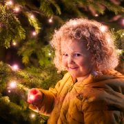 An image of a young girl stood by a lit up Christmas tree