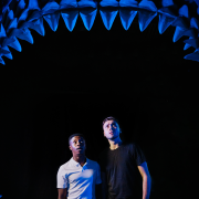 Two men stood underneath model shark jaws looking upwards with shocked expressions
