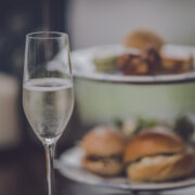 A glass of prosecco in the foreground with afternoon tea in the background